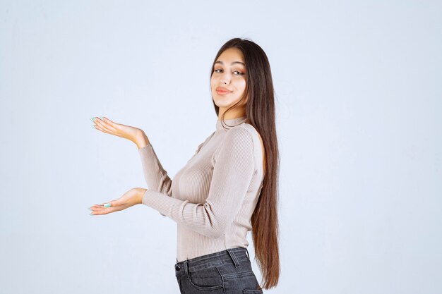 Chica con camisa gris mostrando algo en la mano.