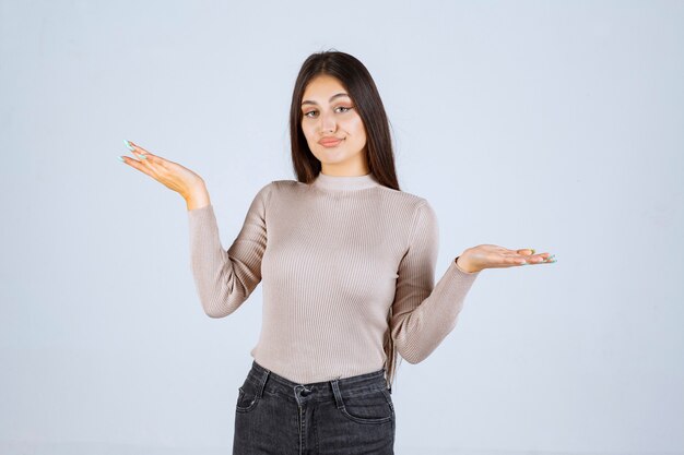 Chica con camisa gris mostrando algo en la mano.