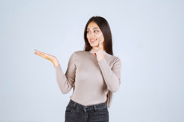 Chica con camisa gris mostrando algo en la mano.