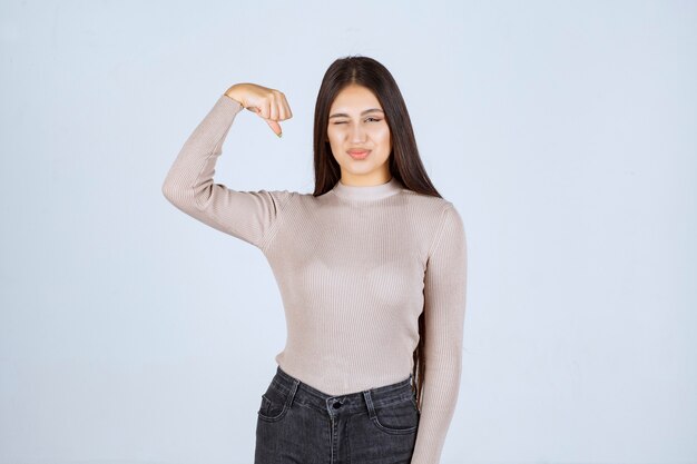 Chica en camisa gris mostrando los músculos de su brazo.