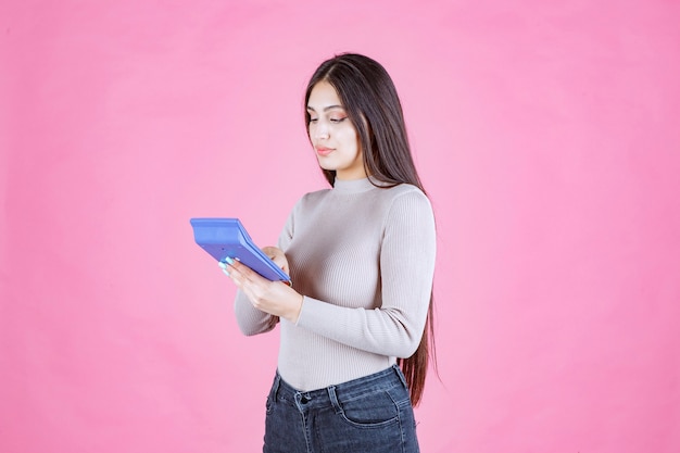 Chica en camisa gris sosteniendo una calculadora azul, mirando y trabajando con ella