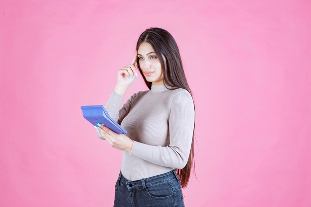 Chica en camisa gris sosteniendo una calculadora azul y pensando en los detalles