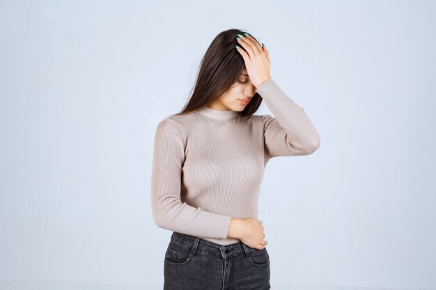 Chica en camisa gris sosteniendo su cabeza debido a dolor de cabeza.