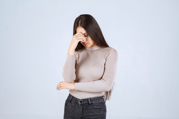 Chica en camisa gris sosteniendo su cabeza debido a dolor de cabeza.