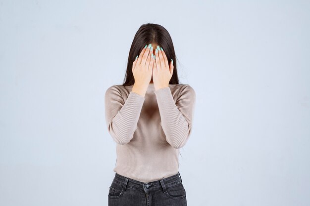 Chica en camisa gris sosteniendo su cabeza debido a dolor de cabeza.