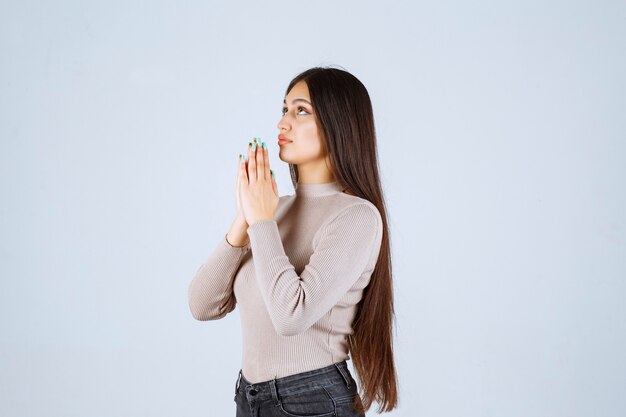 Chica en camisa gris uniendo sus manos y rezando.