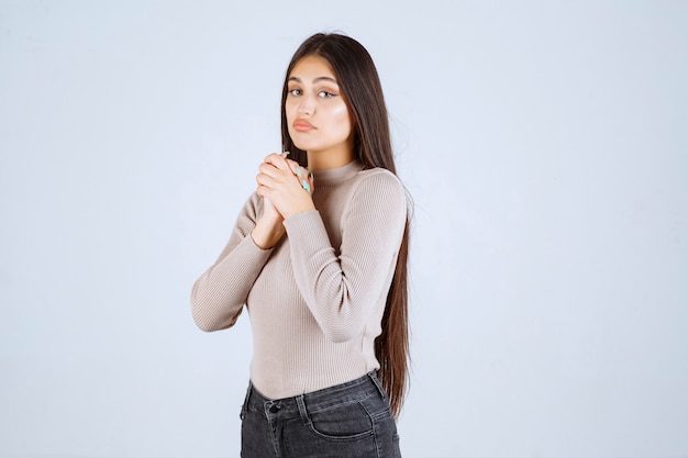 Chica en camisa gris uniendo sus manos y rezando.