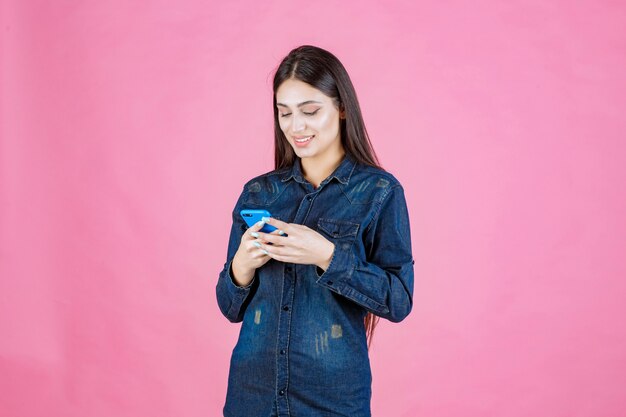 Chica en una camisa de mezclilla charlando en su teléfono inteligente