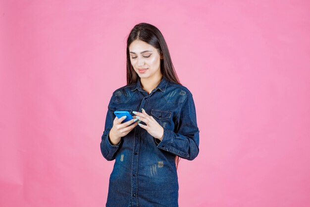 Chica en una camisa de mezclilla charlando en su teléfono inteligente