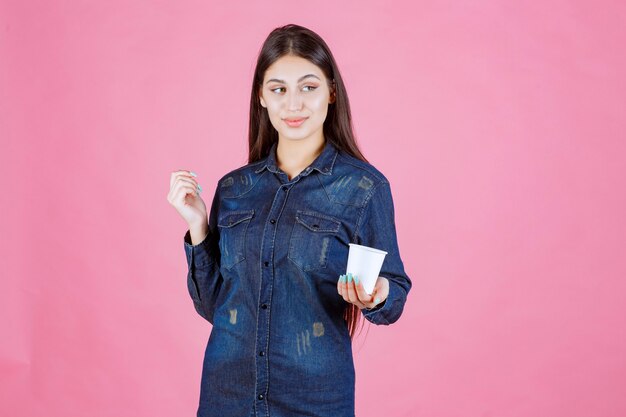 Chica en camisa de mezclilla ofreciendo una taza de café a su amiga