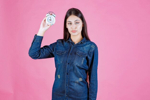 Chica en camisa de mezclilla sosteniendo y promocionando un despertador