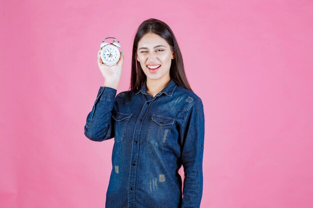 Chica en camisa de mezclilla sosteniendo un reloj despertador y promoviéndolo