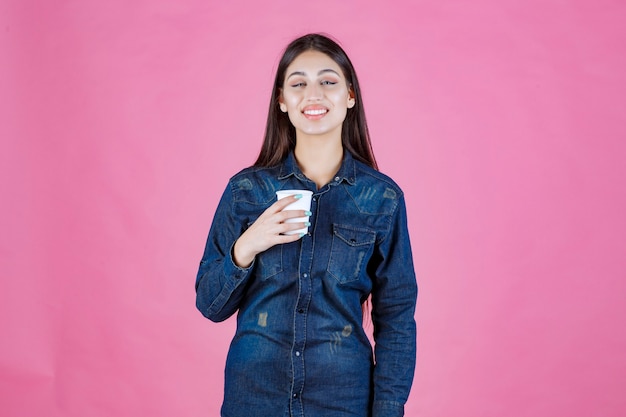 Chica en camisa de mezclilla sosteniendo una taza de café y se siente positiva