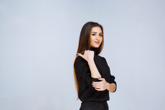 Chica con camisa negra apuntando a algo a la izquierda. Foto de alta calidad