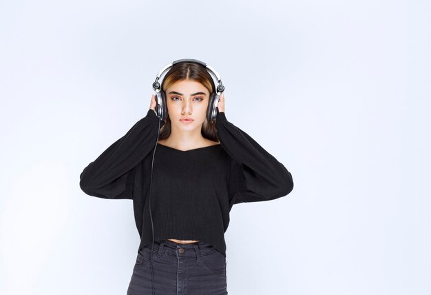 Chica de camisa negra con auriculares y escuchando música. Foto de alta calidad