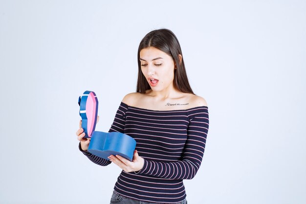 Chica con camisa a rayas abre una caja de regalo azul y se sorprende.