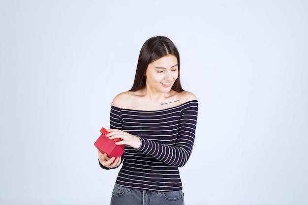 Chica con camisa a rayas abre una caja de regalo roja y se pone feliz.
