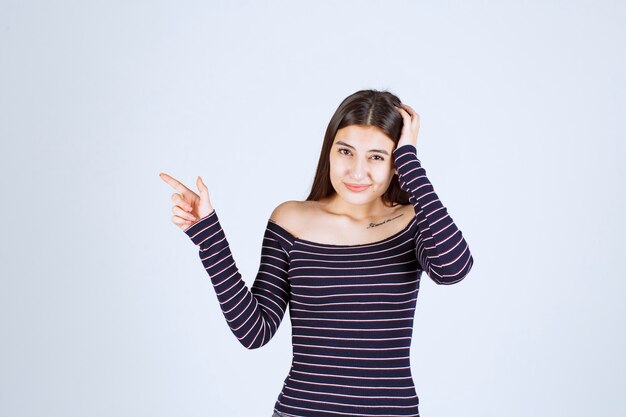 Chica con camisa a rayas apuntando a algo a la izquierda.