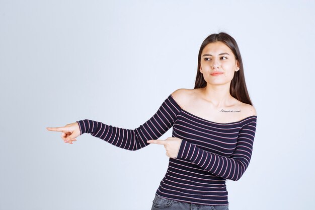 Chica con camisa a rayas apuntando a algo a la izquierda.