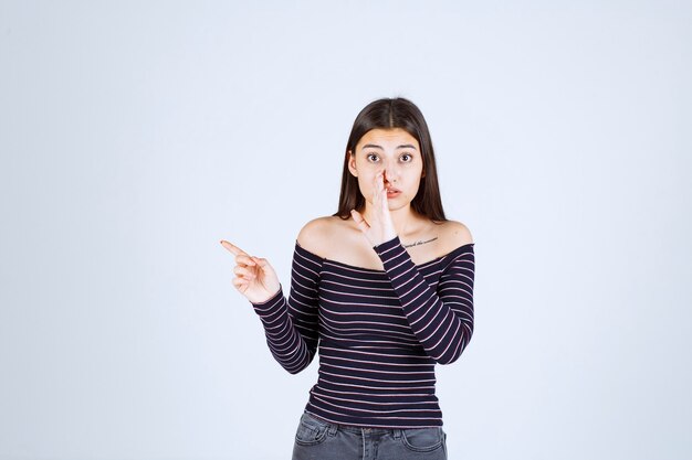 Chica con camisa a rayas apuntando a alguien del lado izquierdo.