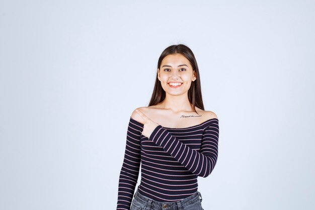 Chica con camisa a rayas apuntando a alguien del lado izquierdo.