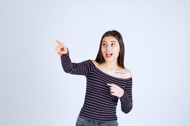 Chica con camisa a rayas apuntando a alguien del lado izquierdo.