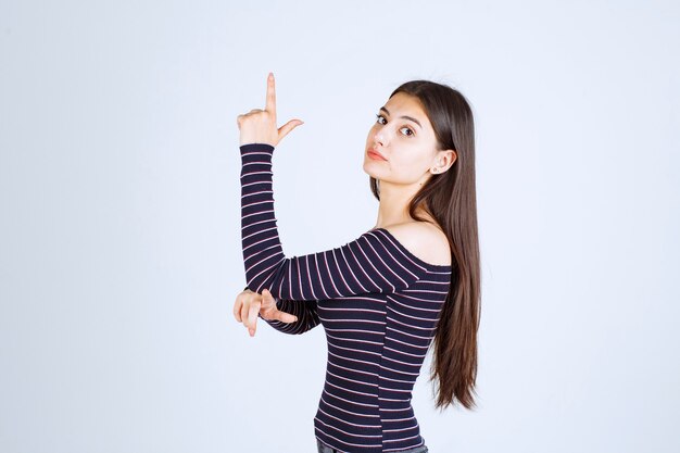 Chica en camisa a rayas apuntando hacia arriba y mostrando emociones.