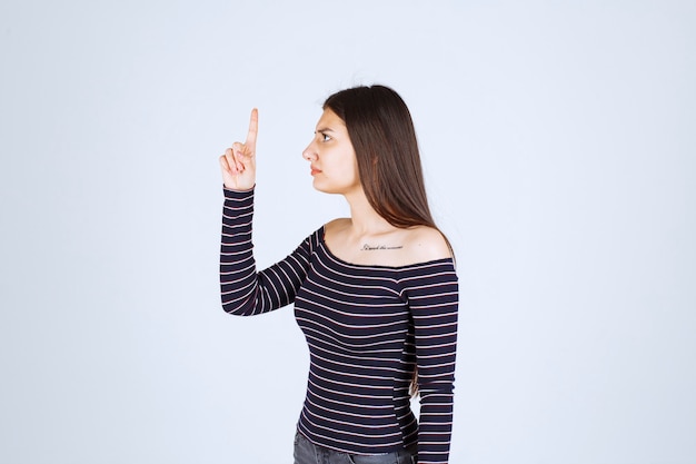 Foto gratuita chica en camisa a rayas apuntando hacia arriba y mostrando emociones.