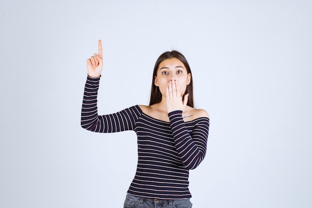 Foto gratuita chica en camisa a rayas apuntando hacia arriba y mostrando emociones.