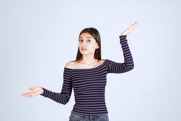 Chica en camisa a rayas apuntando hacia arriba y mostrando emociones.