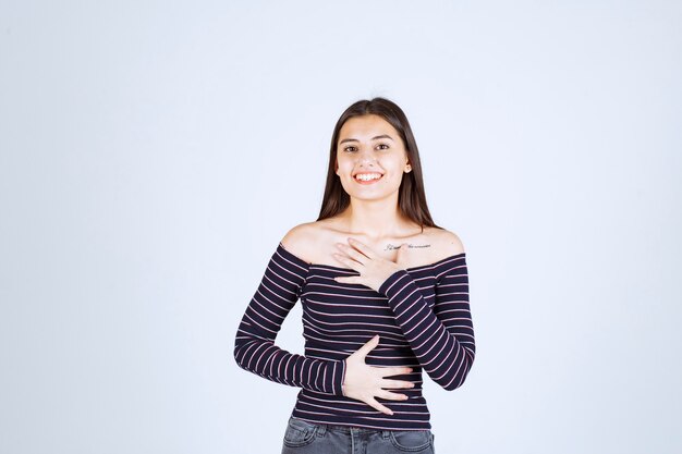 Chica en camisa a rayas apuntando a sí misma.