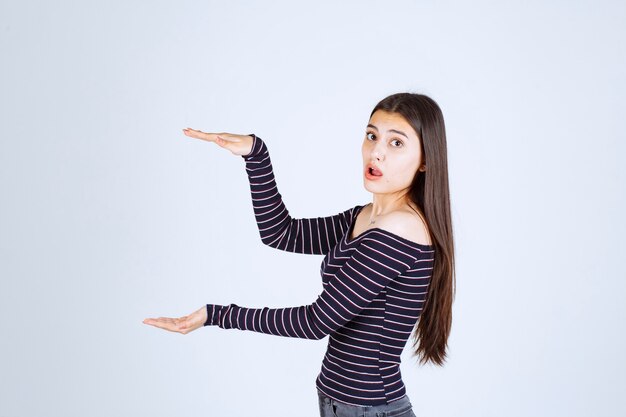 Chica en camisa de rayas mostrando la medida o cantidad estimada de un producto.