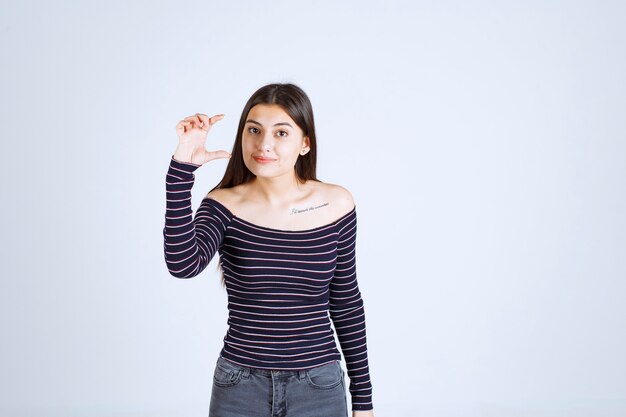Chica en camisa de rayas mostrando la medida o cantidad estimada de un producto.