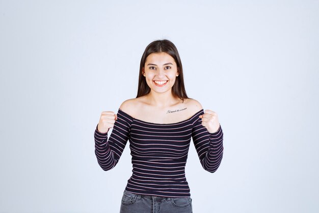 Chica en camisa a rayas mostrando los músculos de su brazo.