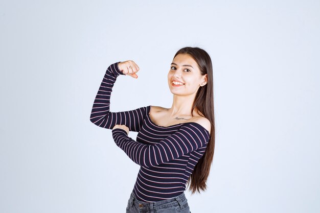 Chica en camisa a rayas mostrando los músculos de su brazo.