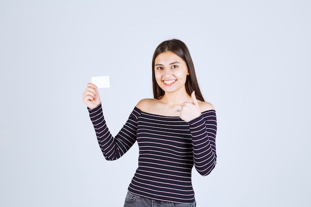 Chica en camisa a rayas presentando su tarjeta de visita con confianza.