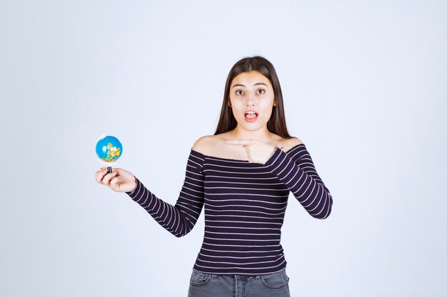 Chica en camisa a rayas sosteniendo un mini globo y apuntando a él.