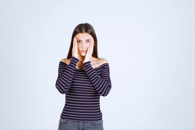 Chica con camisa a rayas sosteniendo su cabeza porque está agotada o tiene dolor de cabeza.