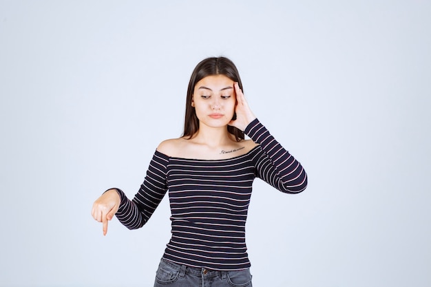 Chica con camisa a rayas sosteniendo su cabeza porque está agotada o tiene dolor de cabeza.