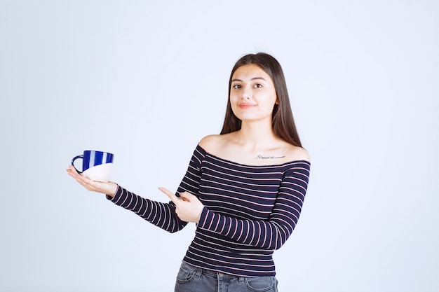 Chica en camisa a rayas sosteniendo una taza de café y mostrando signo de disfrute.