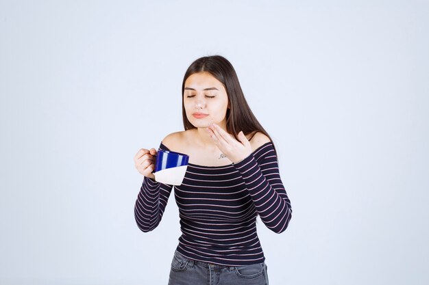 Chica en camisa a rayas sosteniendo una taza de café y oliéndola.