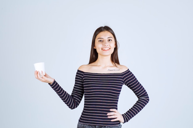 Foto gratuita chica en camisa a rayas sosteniendo una taza de café de plástico y parece positiva.