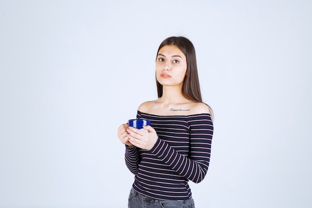 Chica en camisa a rayas sostiene una taza de café y parece confundida.