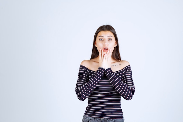 La chica con camisa a rayas se ve confundida y emocionada.