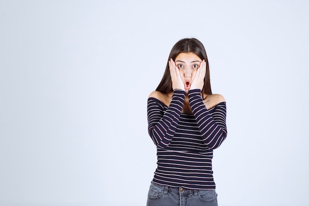 La chica con camisa a rayas se ve confundida y emocionada.