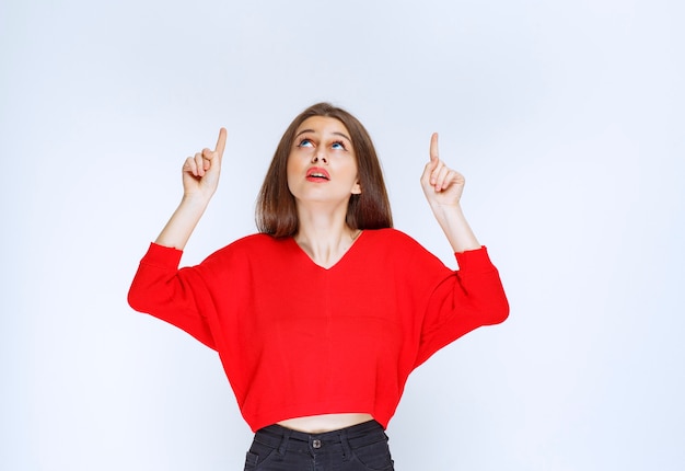 Chica de camisa roja apuntando al revés.