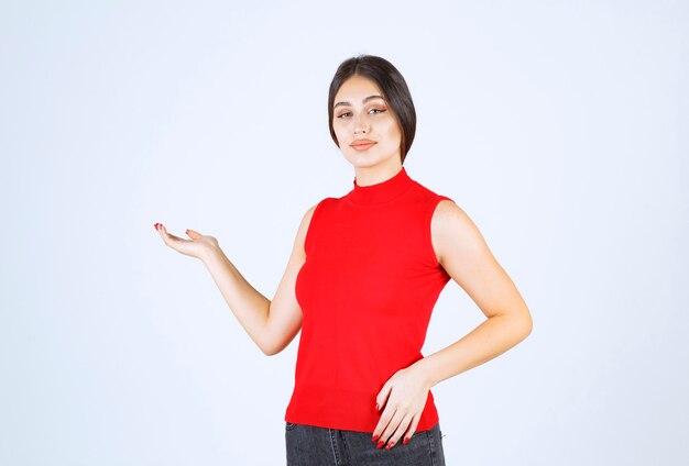 Chica con camisa roja apuntando a algo a la izquierda.