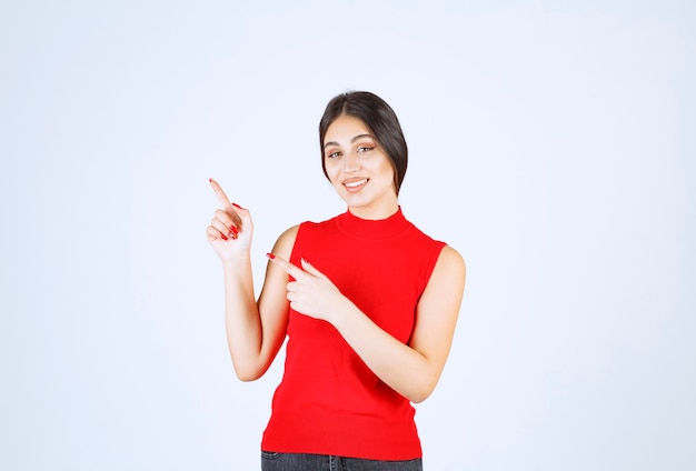 Chica con camisa roja apuntando a algo a la izquierda.