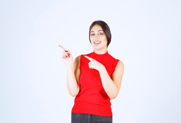 Chica con camisa roja apuntando a algo a la izquierda.