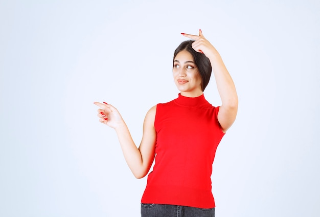 Chica con camisa roja apuntando a algo a la izquierda.